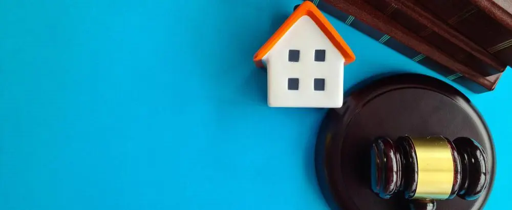 Model house beside a judge's gavel and law books on a blue background